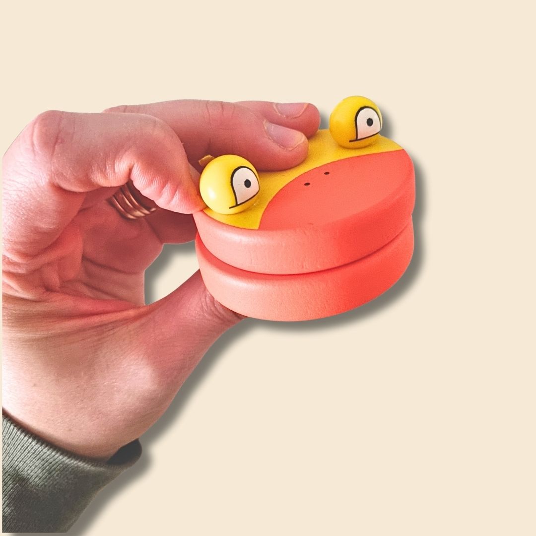 Hand holding a small, yellow and orange duck shaped wooden castanet, on a beige background