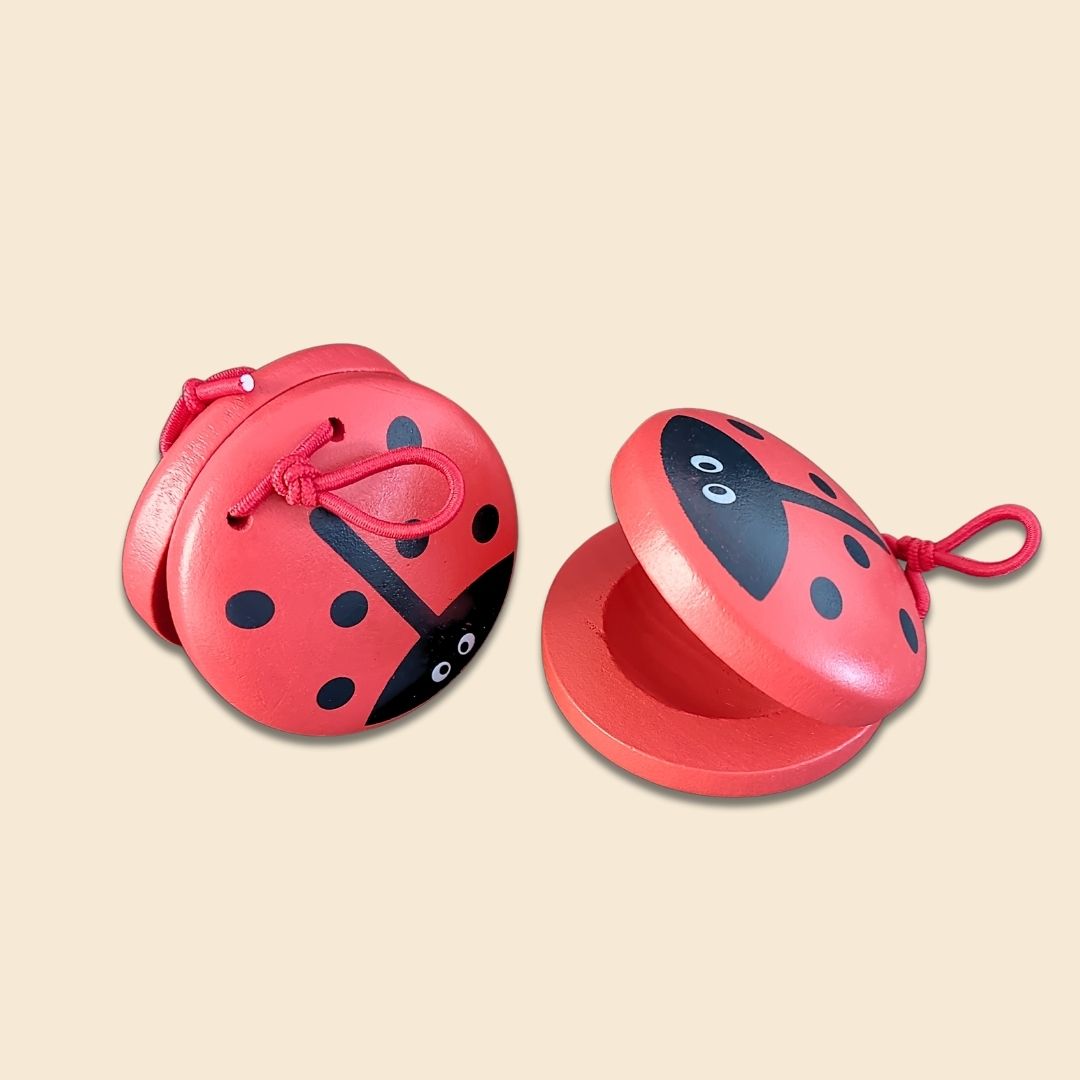 Two red ladybug-shaped castanets on a beige background, showing both sides of the musical instrument