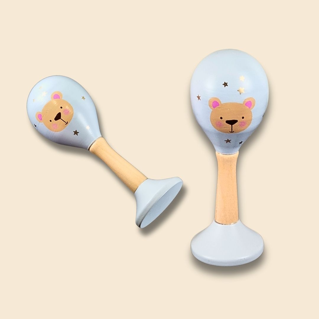 Two light grey baby rattles with bear faces on a beige background