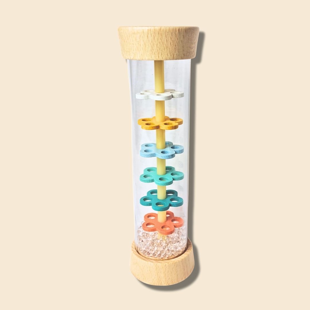 Colourful flower-shaped interior of wooden rainstick musical instrument with transparent tube and wooden base and top on a beige background. Clear acrylic beads create rain sound.