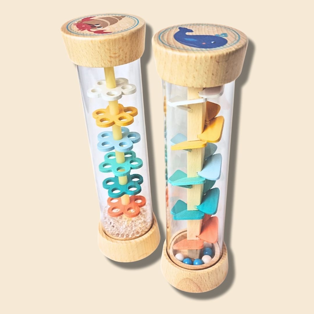 Two colourful wooden rainstick musical toys with transparent tubes and wooden ends on a beige background