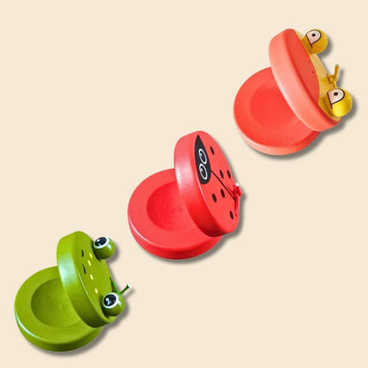 3 single castanets of different animal types: green frog, red ladybug and orange/yellow duck - on a beige background. 