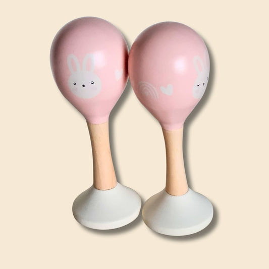 Two pink maracas with bunny faces on a beige background
