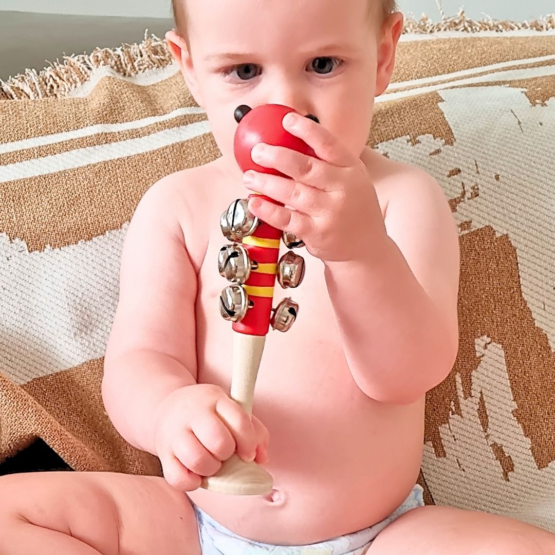 Baby boy holding a red ladybug bell stick instrument sitting on a textured lounge